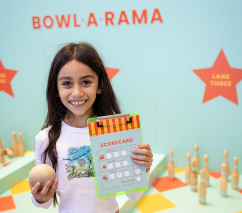 A girl holding up her game card from Bowl-A-Rama 