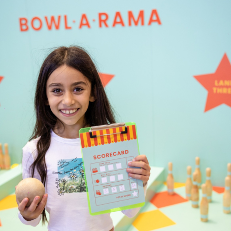 A girl holding up her game card from Bowl-A-Rama 
