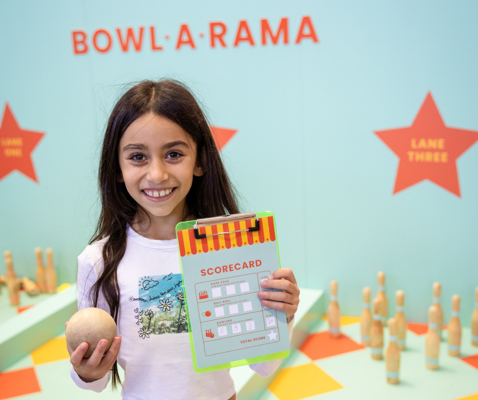 A girl holding up her game card from Bowl-A-Rama